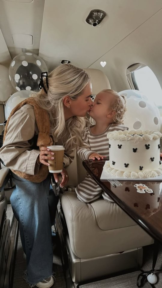 Una madre y su niño pequeño se besan en un jet privado; Un pastel de cumpleaños se encuentra en una mesa cercana.