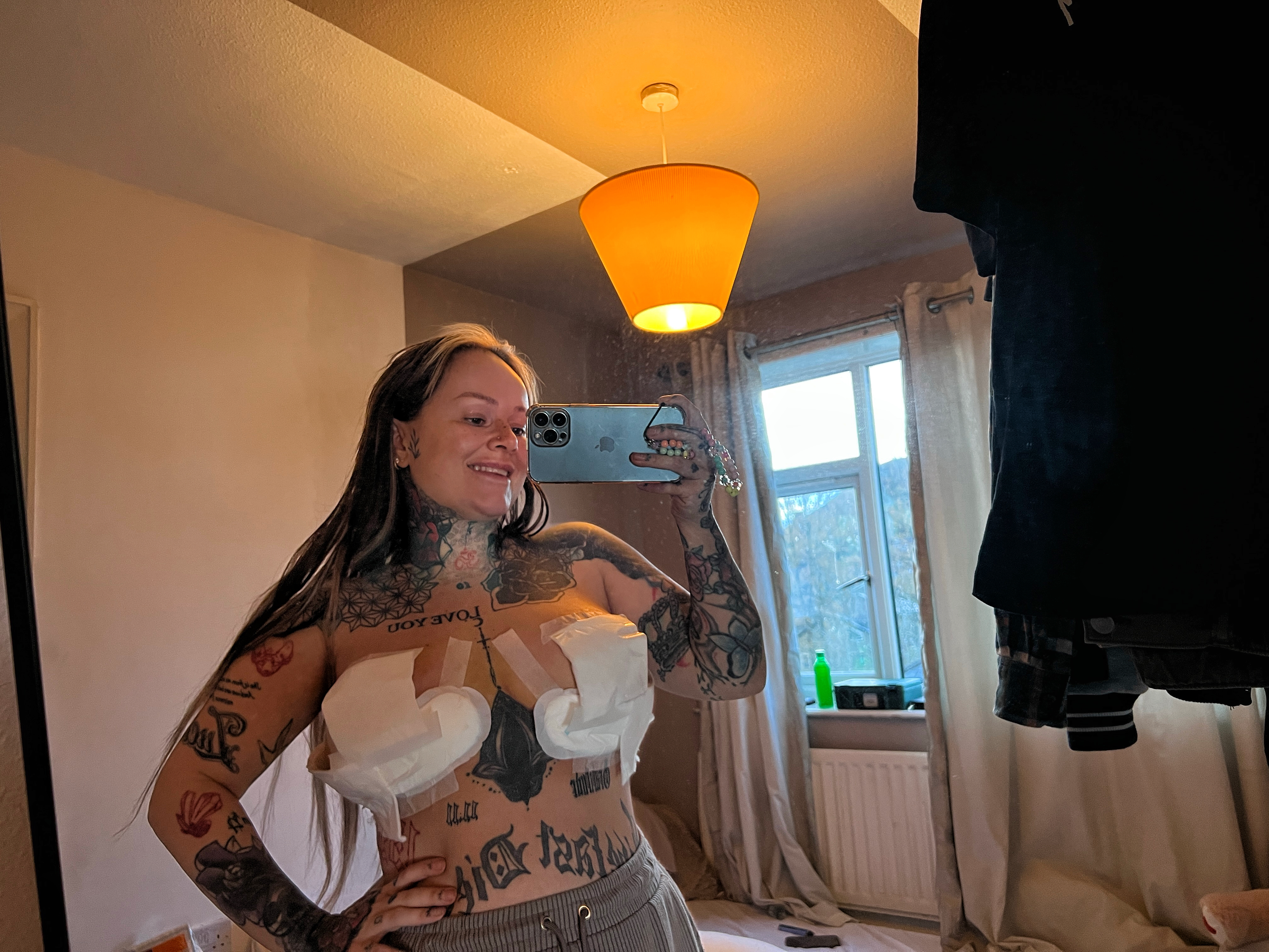 Mujer con tatuajes tomando una selfie después de la cirugía de reducción de senos.