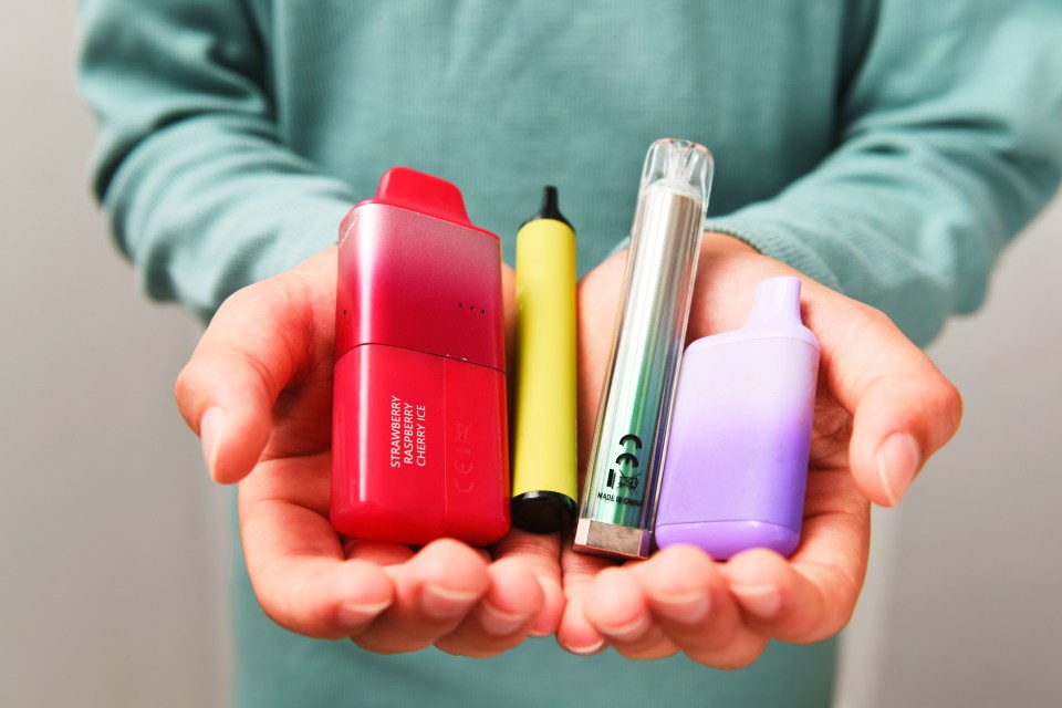Las manos de un adolescente sosteniendo varios vapos desechables.