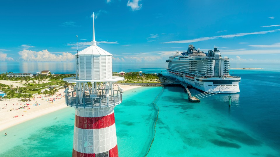 Vista aérea de un crucero atracado cerca de un faro y playa.