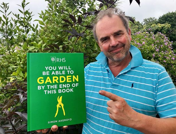 Una foto de un hombre con una camisa azul y sosteniendo un libro verde