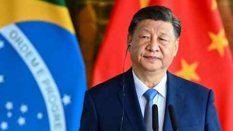 Xi Jinping se encuentra en un podio con un auricular frente a las banderas brasileñas y chinas durante una conferencia de prensa
