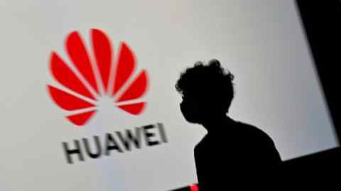 Una persona pasa por una pantalla grande que muestra el logotipo de Huawei