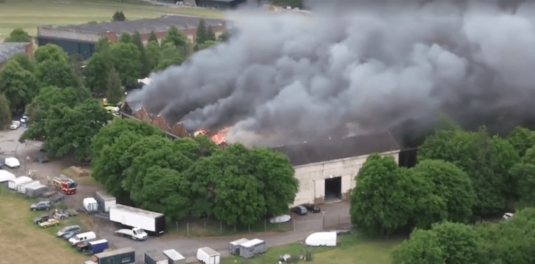 Vista aérea de un gran edificio envuelto en llamas y humo espeso.