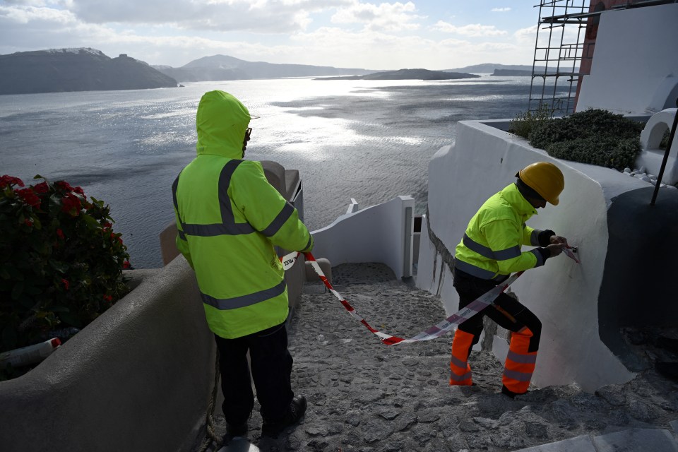 Dos trabajadores en chalecos de seguridad amarillos brillantes reparan un edificio con vistas a un cuerpo de agua.
