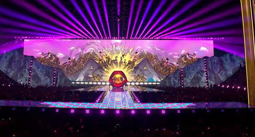 Etapa de concierto con una gran pantalla de video que muestra un paisaje surrealista y labios gigantes.
