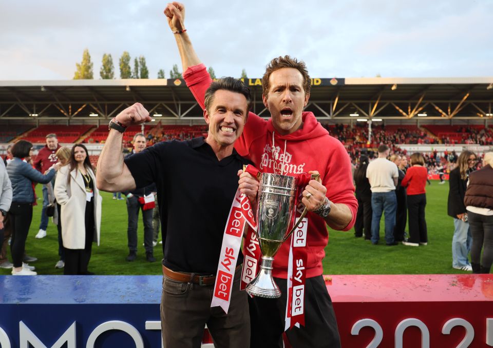 Rob McElhenney y Ryan Reynolds sostienen un trofeo en un juego de fútbol.