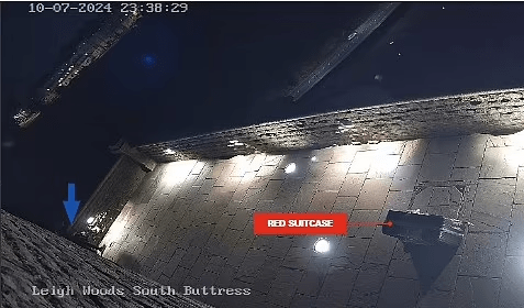 Imagen de cámara de seguridad nocturna de una maleta roja en un patio.