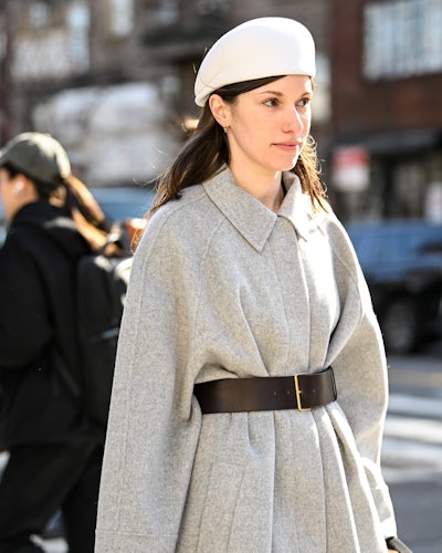 NEW YORK, NEW YORK - 09 FÉVRIER : Laura Reilly porte un manteau gris, une ceinture noire, un sac crème, avec...