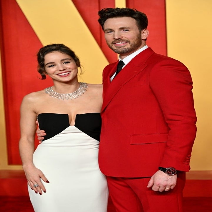 Chris Evans en costume rouge et Alba Baptista en robe bustier noire et blanche, souriant ensemble sur le tapis rouge