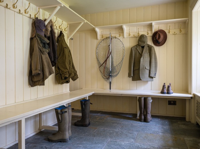 une pièce avec un filet de pêche et des manteaux et chapeaux suspendus ;  bottes en caoutchouc soigneusement disposées sur le sol