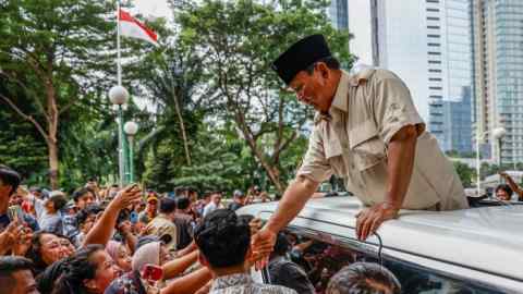 Prabow Subianto se penche hors du toit ouvrant d'une voiture pour serrer la main d'un membre d'une foule de supporters
