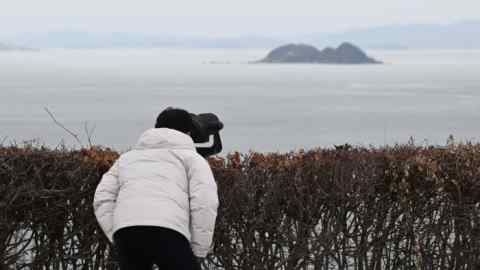 Un homme regarde avec des jumelles la côte nord-coréenne depuis un point de vue en Corée du Sud