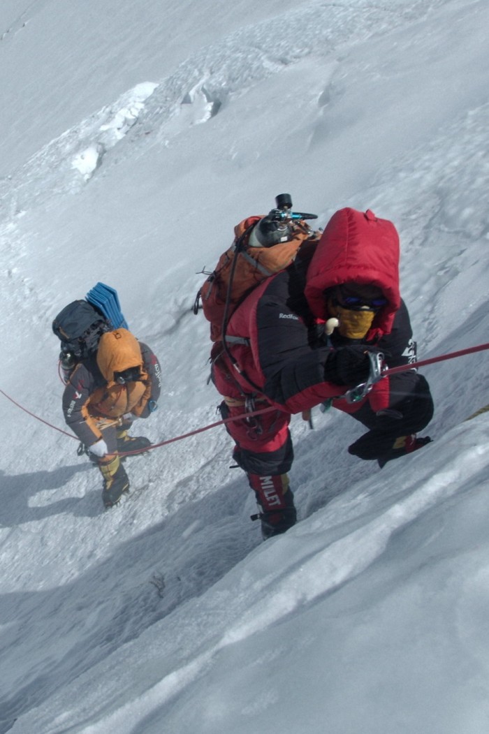Deux alpinistes vêtus de lourdes couches d'hiver escaladent une pente raide et glacée à l'aide de cordes