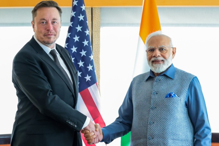 Elon Musk, à gauche, serre la main de Narendra Modi avec les drapeaux américain et indien en arrière-plan