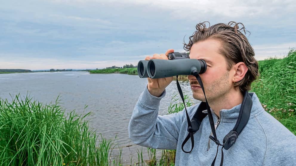 Un homme regarde dans un télescope sur les rives de l’Oder