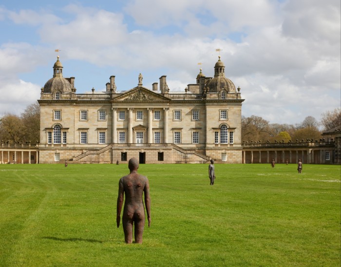 Statues en fonte représentant des personnages dans un champ herbeux avec un manoir en arrière-plan. La statue au premier plan semble avoir les pieds enfouis dans le sol