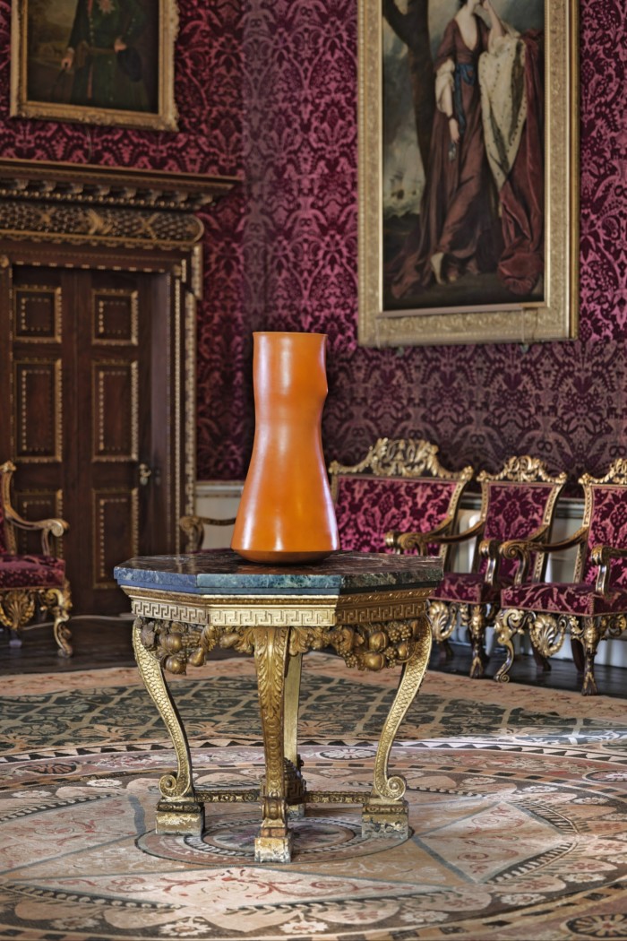 Une sculpture orange sur une table dans une pièce avec des meubles ornés et anciens