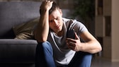 Image symbolique : Un jeune homme regarde avec inquiétude son smartphone.