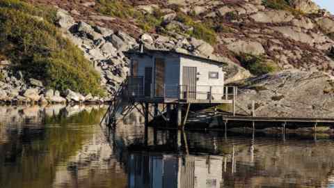 petite cabane de sauna en bois surplombant un lac devant des rochers