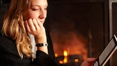 Jeune femme lisant avec un e-book près de la cheminée.  La question se pose de savoir quels sont les meilleurs lecteurs de livres électroniques en comparaison