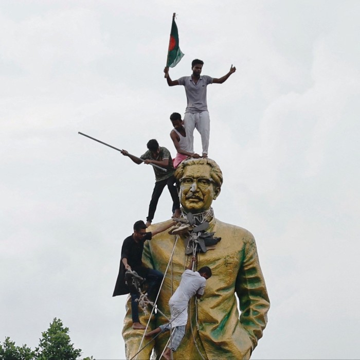 Des gens escaladent la statue de Cheikh Mujibur Rahman alors qu'ils célèbrent la démission de Cheikh Hasina lundi