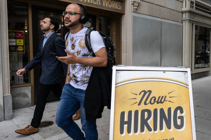 Des gens passent devant un restaurant avec un panneau « recrutement en cours » à l'extérieur, à Washington, DC