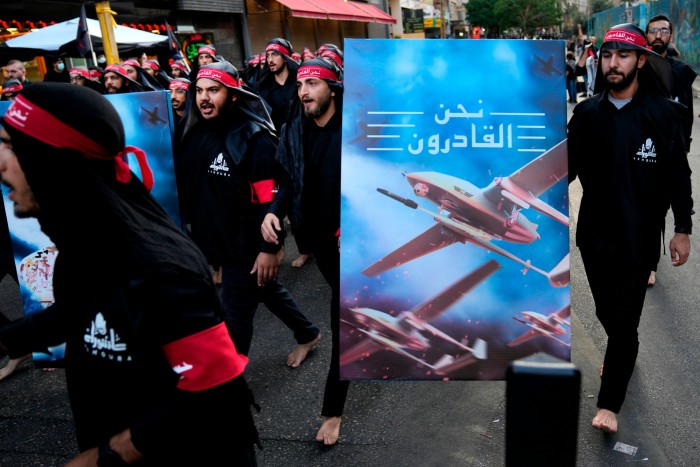 Des membres du Hezbollah marchent pieds nus dans le sud de Beyrouth, portant une affiche montrant des drones du Hezbollah avec les mots en arabe « Nous arrivons ».