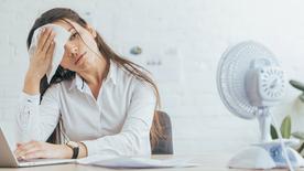 Une femme est assise à son bureau, en sueur, et s'essuie le front.