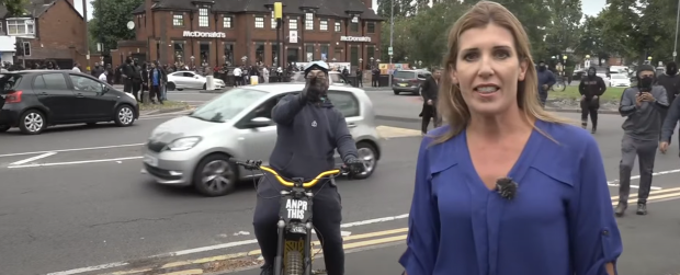 Un manifestant masqué s'approche d'un journaliste de Sky News lors d'un reportage en direct