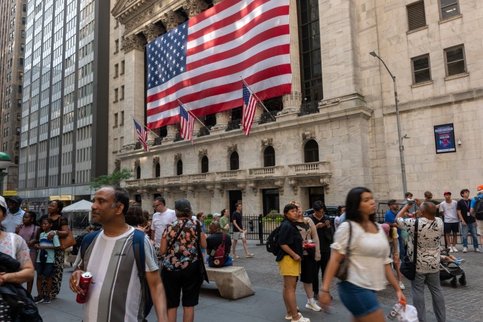 Des gens marchent devant la Bourse de New York avec un immense drapeau américain accroché à l'extérieur