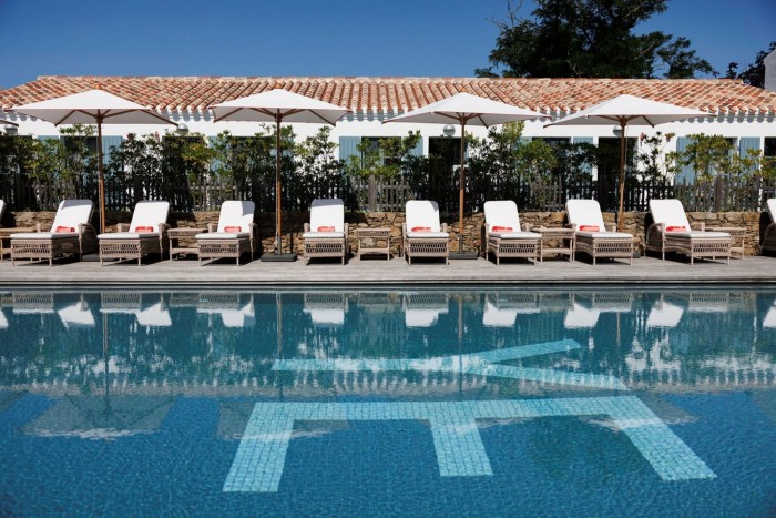 Neuf chaises longues alignées sous des parasols au bord d'une piscine