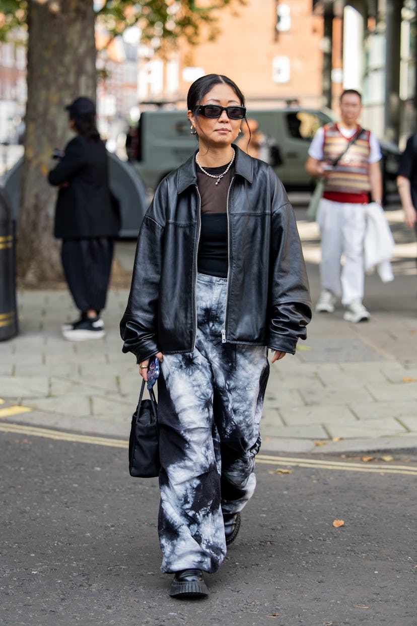 Un invité porte une veste en cuir noir, un pantalon noir et blanc, une chemise et un sac à l'extérieur de Yuhan Wang pendant le London F...