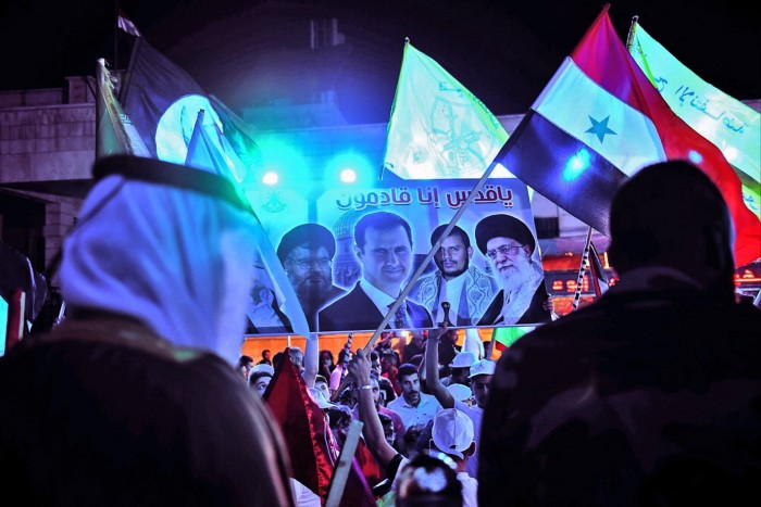 Des Syriens brandissent des drapeaux et brandissent une pancarte représentant Hassan Nasrallah, le président syrien Bashar al-Assad, le dirigeant houthi du Yémen Abdulmalik al-Houthi et le guide suprême iranien l'ayatollah Ali Khamenei, lors d'un rassemblement en 2021.