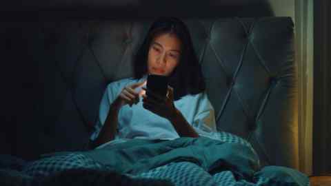 Une femme regarde son téléphone de travail au lit