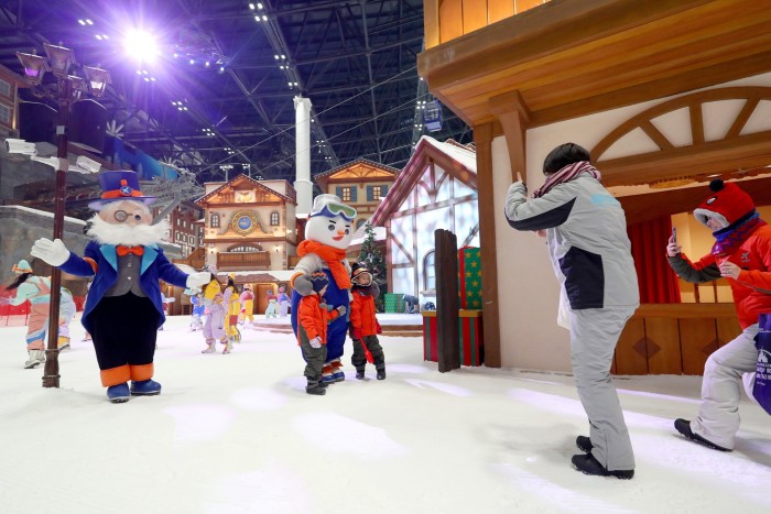 Une femme prend une photo de deux enfants à côté de quelqu’un en costume de bonhomme de neige 