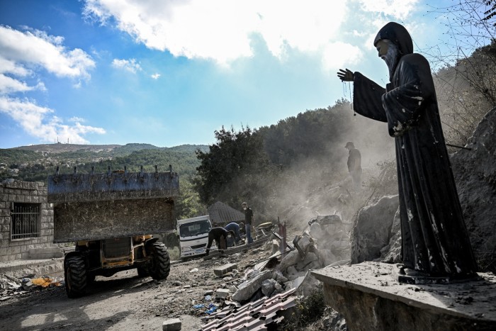 Une statue du saint chrétien maronite Mar Charbel du XIXe siècle est représentée alors qu'un bulldozer se déplace pour nettoyer les décombres et les débris du site d'une précédente frappe aérienne israélienne sur le village d'Aito, dans le nord du Liban, le 15 octobre.