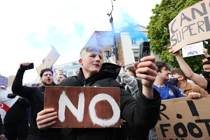 Un fan de football devant une manifestation tient une fusée éclairante et une pancarte disant « Non » 