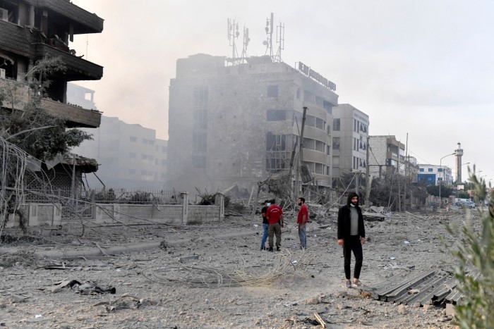 Des personnes debout dans une rue près de bâtiments endommagés suite à une frappe aérienne israélienne dans le quartier de Dahieh à Beyrouth, au Liban, le 6 octobre 2024.