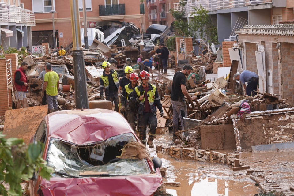 Les pompiers marchent tandis que les gens tentent de réparer les dégâts après les inondations