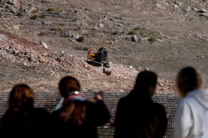 La population locale se tient le long de la barrière de sécurité et regarde un bulldozer israélien opérer dans la zone tampon qui sépare le plateau du Golan sous contrôle israélien de la Syrie.