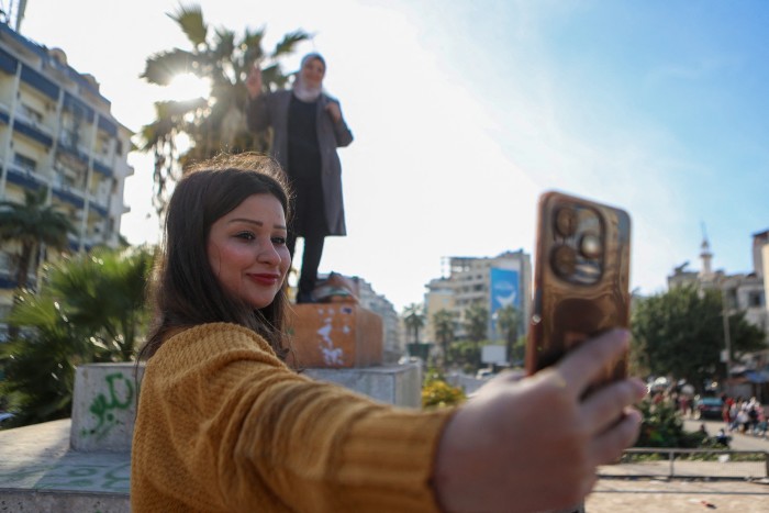 Une femme prend un selfie d'elle et d'un ami debout sur le socle d'une statue renversée de Hafez al-Assad