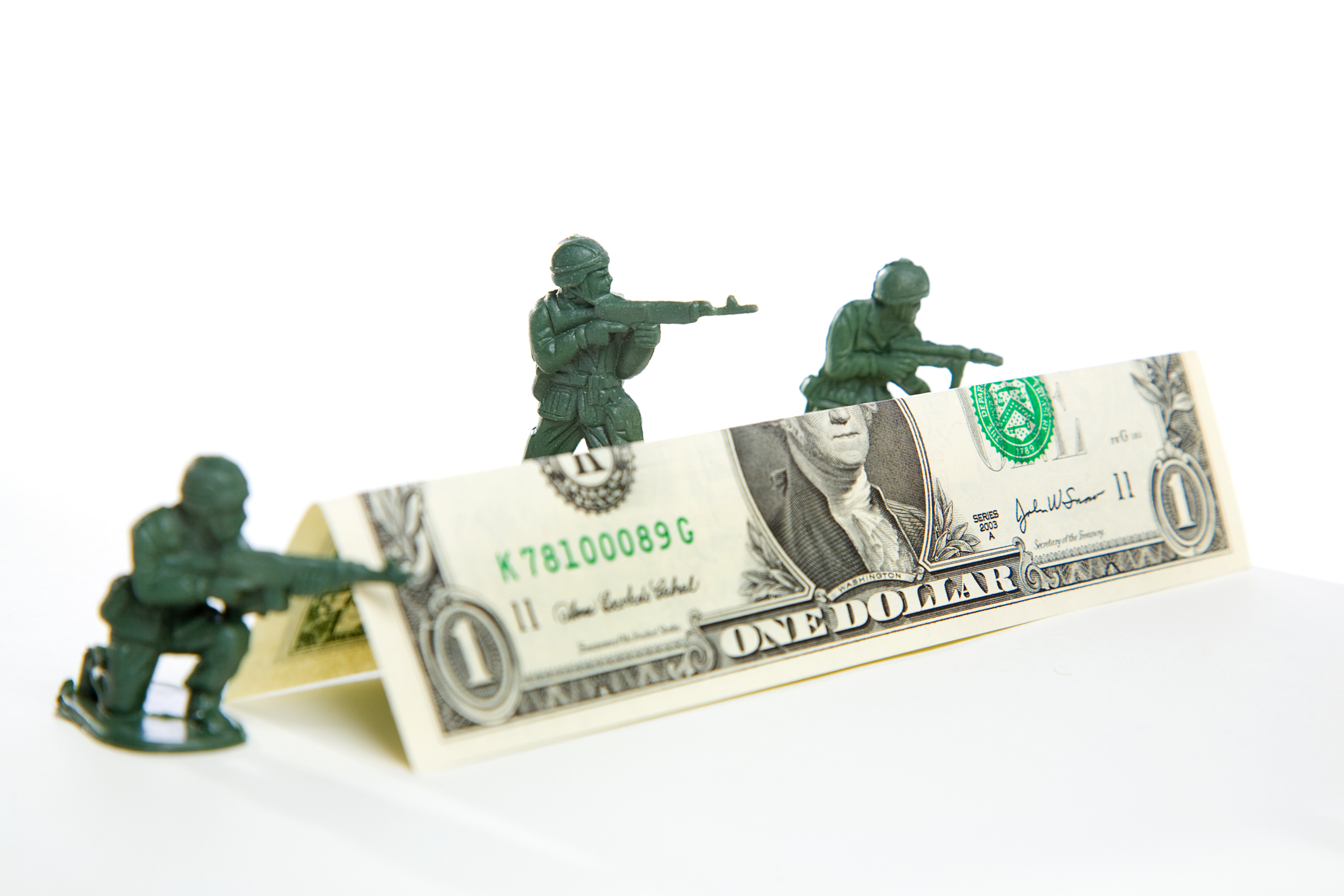Katlanmış bir dolarlık banknottan oluşan bir barikatın üzerinden ateş eden üç plastik oyuncak asker