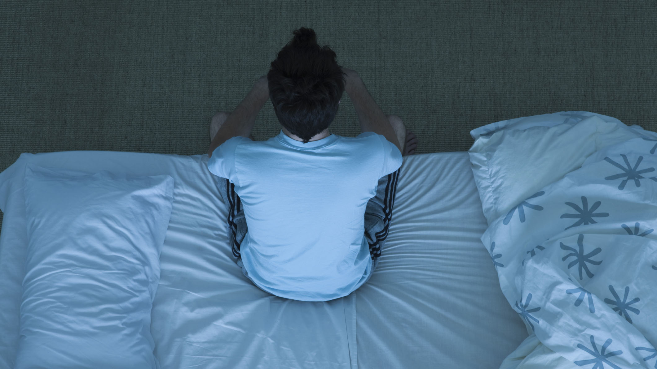 Bir adam yatağının kenarında oturuyor çünkü sadece bir yatak örtüsü üzerinde uyumaktan rahatsız olduğu için uyuyamıyor