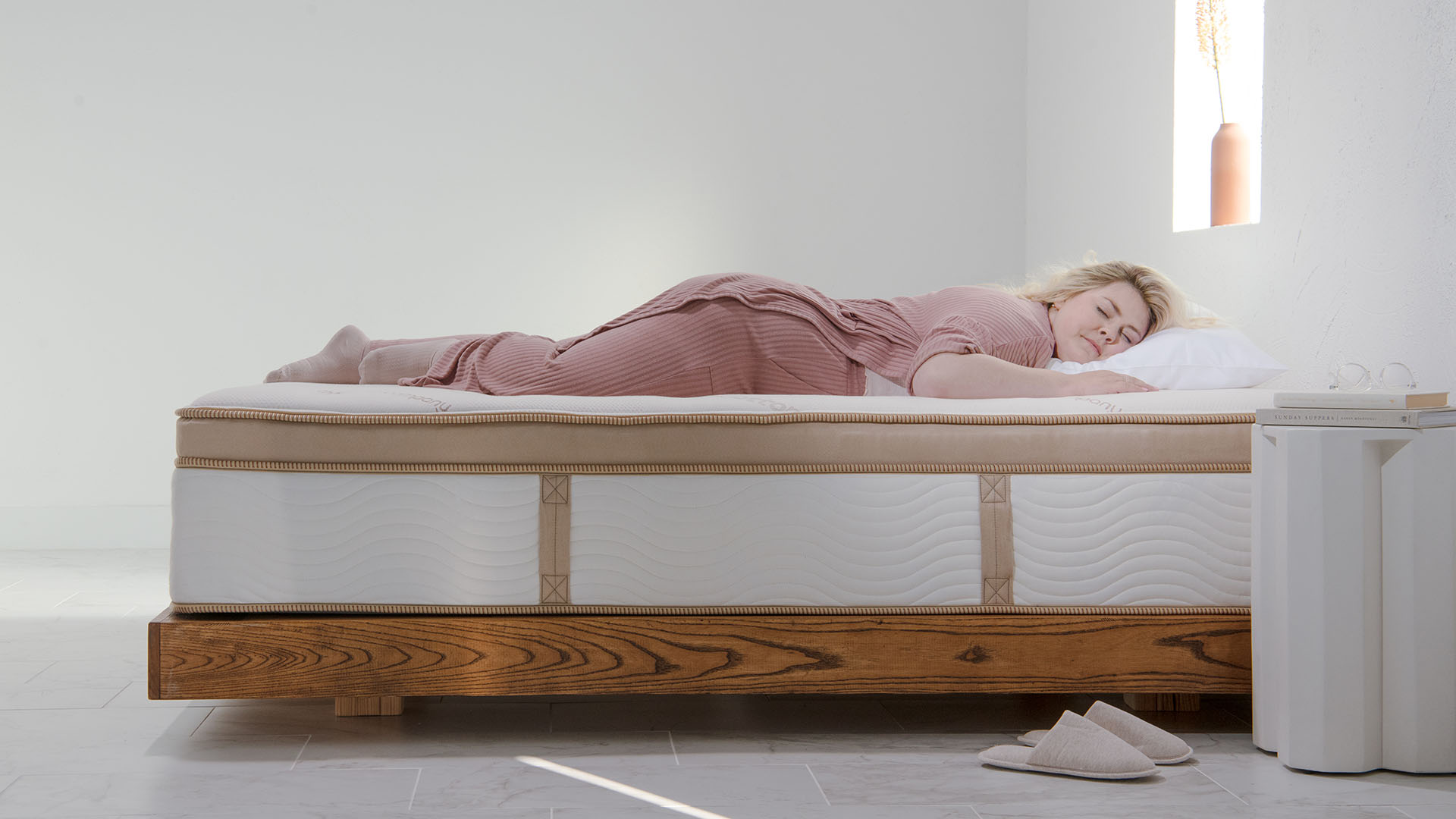 Pembe pijamalı sarı saçlı bir kadın Saatva HD yatağın üzerinde yatıyor