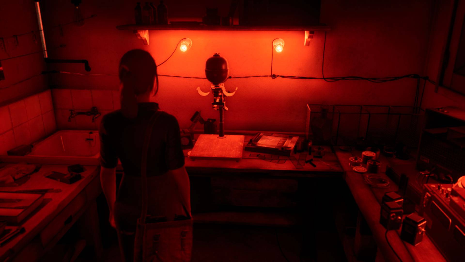 Saçları arkadan bağlı genç bir kadın, önünde kırmızı ışıklı eski ekipmanların bulunduğu bir fotoğraf odasında duruyor.