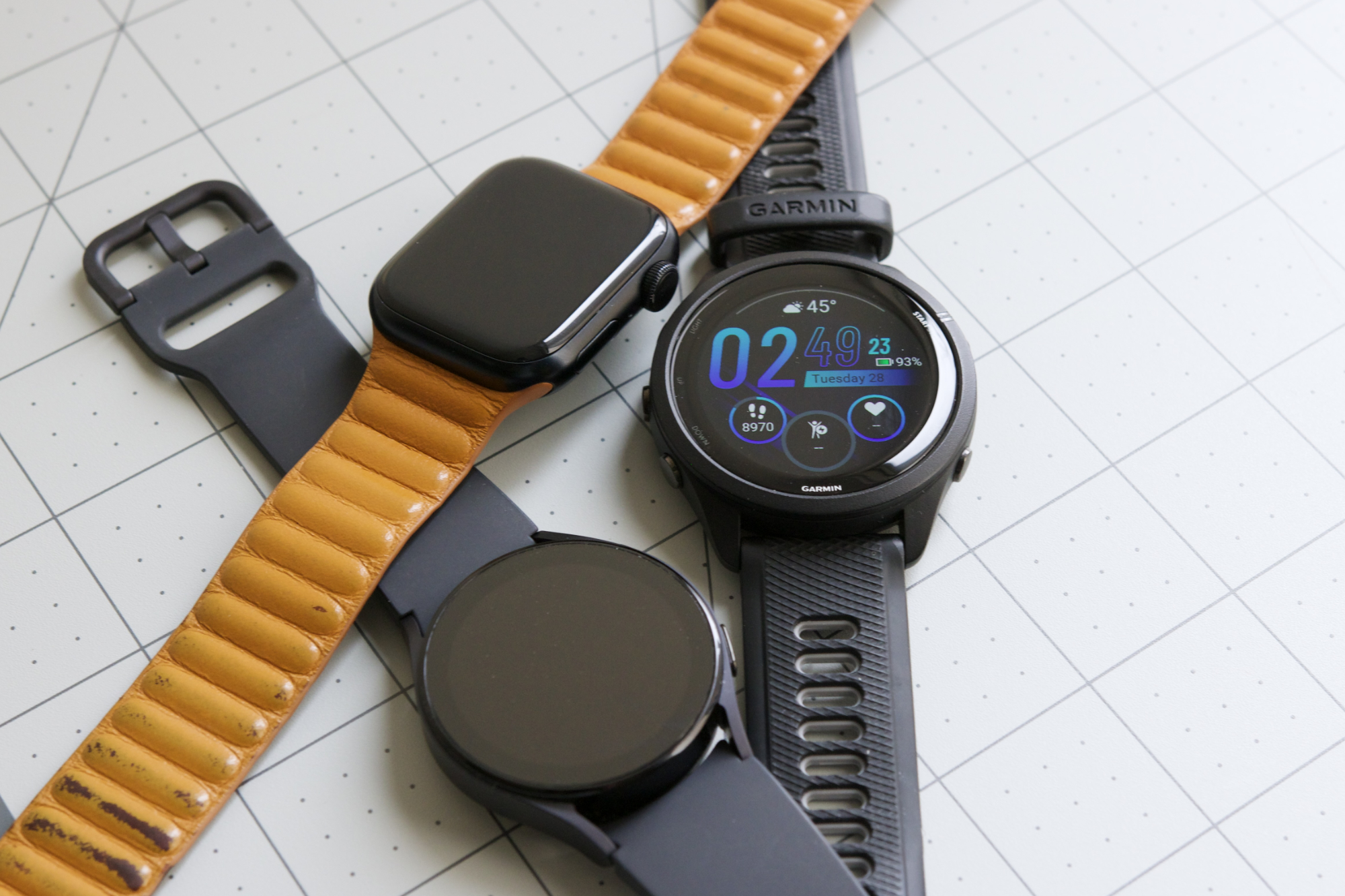 Bir Apple Watch, Galaxy Watch 5 ve Garmin Forerunner 265 masanın üzerinde yan yana duruyor.