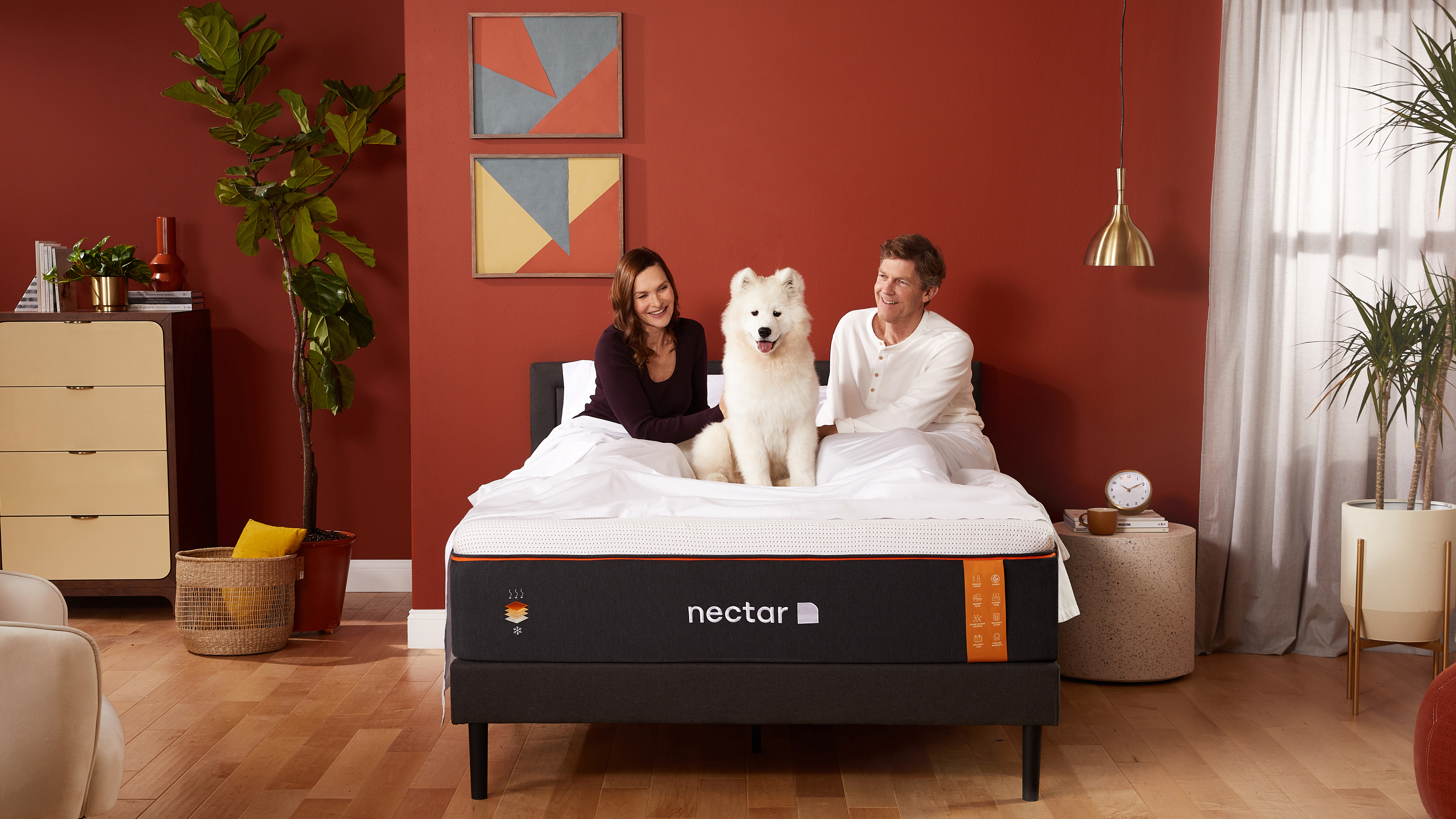 Resimde, markanın en iyi serinletici yatağı olan Nectar Premier Copper Yatak üzerinde oturan genç bir çift ve köpekleri gösterilmektedir.