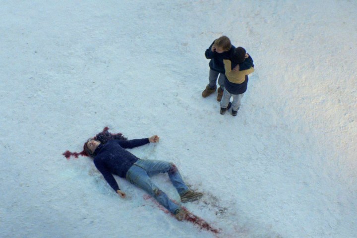 Bir kadın ve oğlan karda ölü bir adama bakıyor.