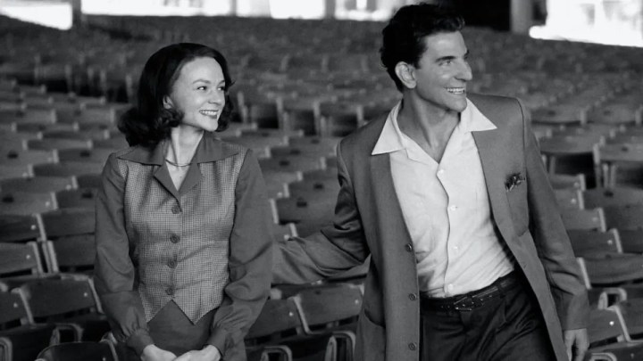 Carey Mulligan and Bradley Cooper as Felicia Montealegre and Leonard Bernstein smiling while looking in the same direction in Maestro.